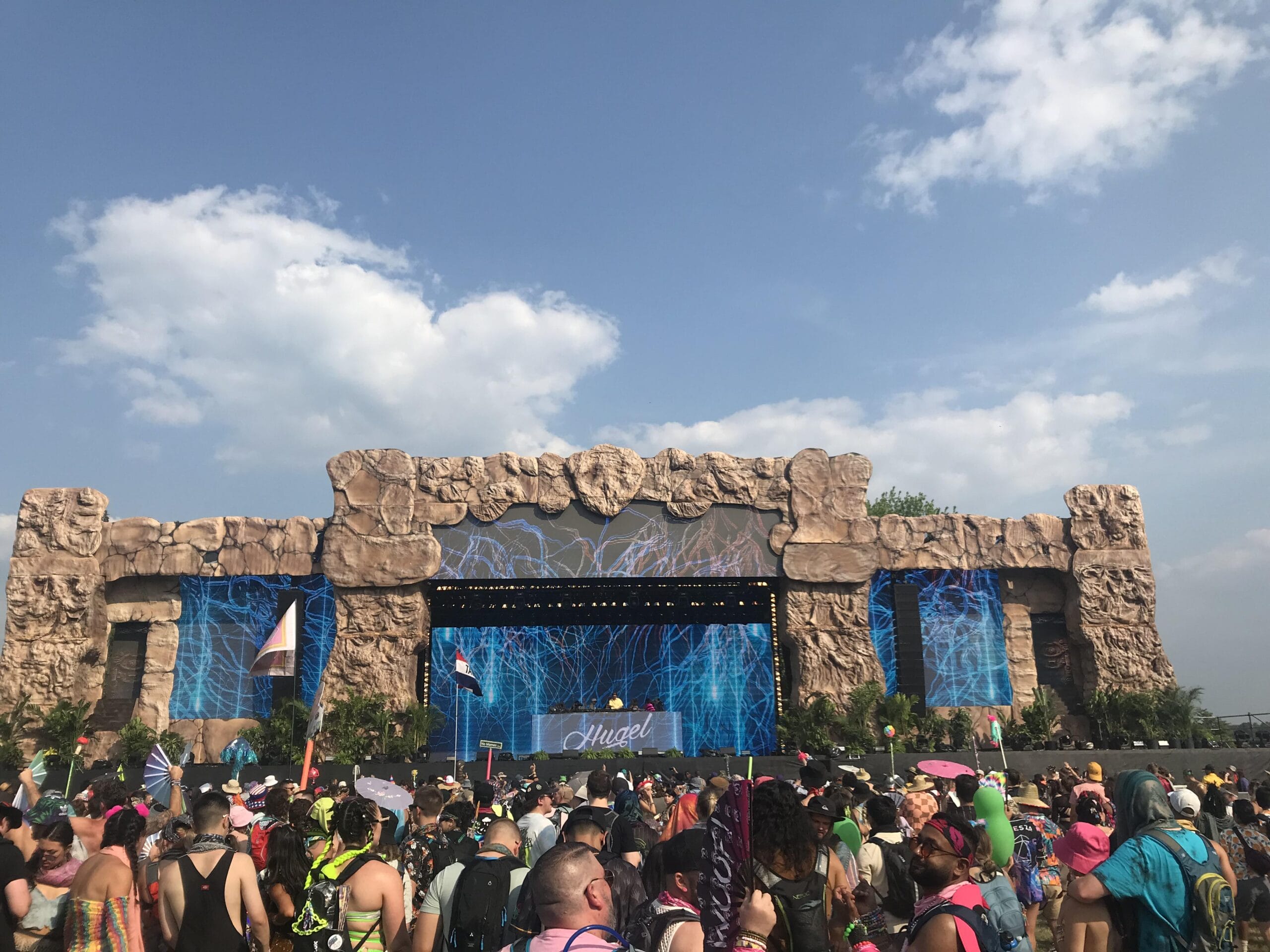 Festival stage with rock facade, large screens, and a crowd of people.