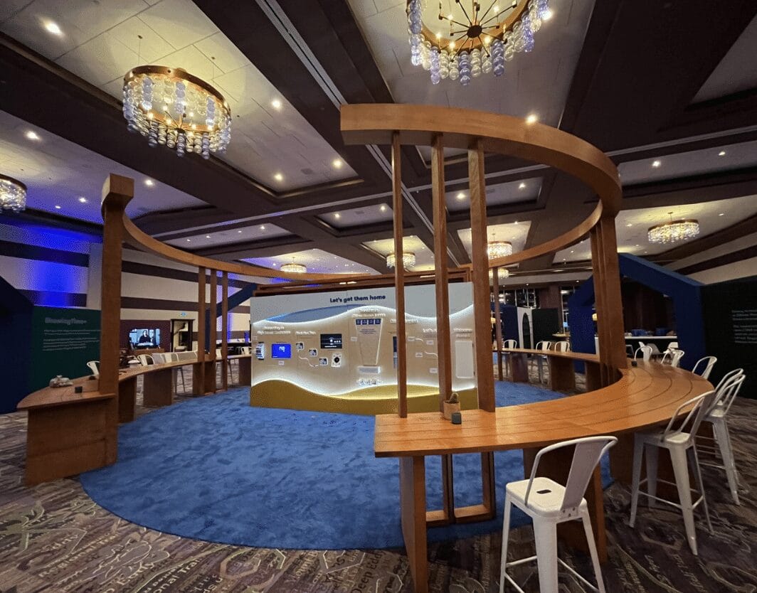 Circular exhibit with wooden structure, blue carpet, and large screen displaying smart home devices.