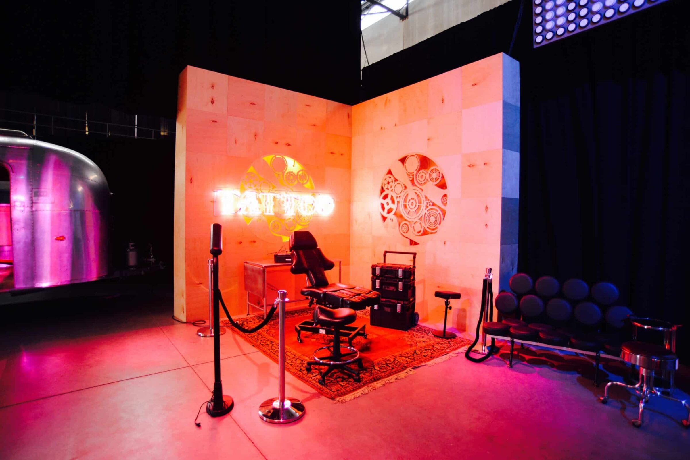 Tattoo parlor setup with neon sign, chair, and Airstream trailer.