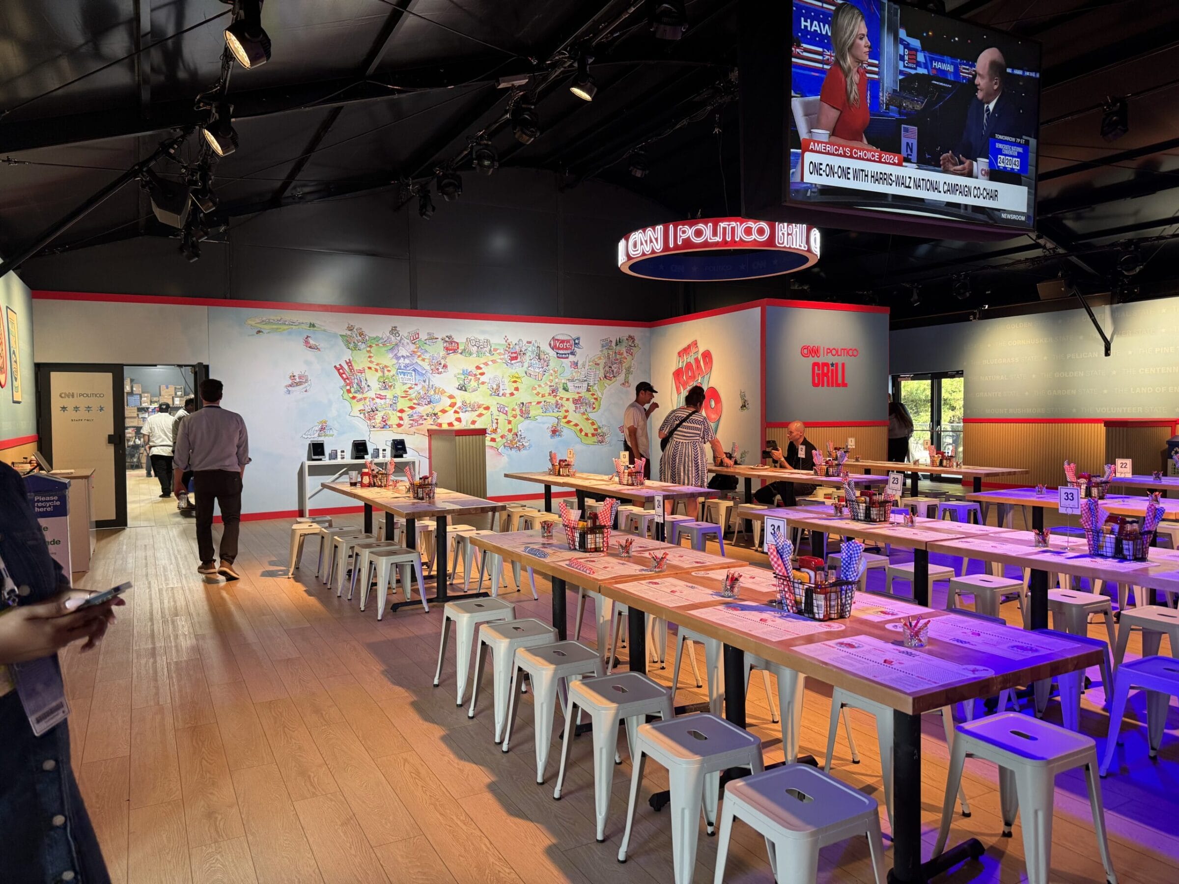 CNN | Politico Grill with tables, a map mural, and a news broadcast on screen.