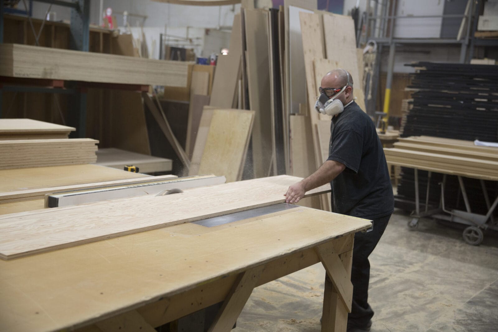 Man in respirator cutting wood on table saw in workshop.