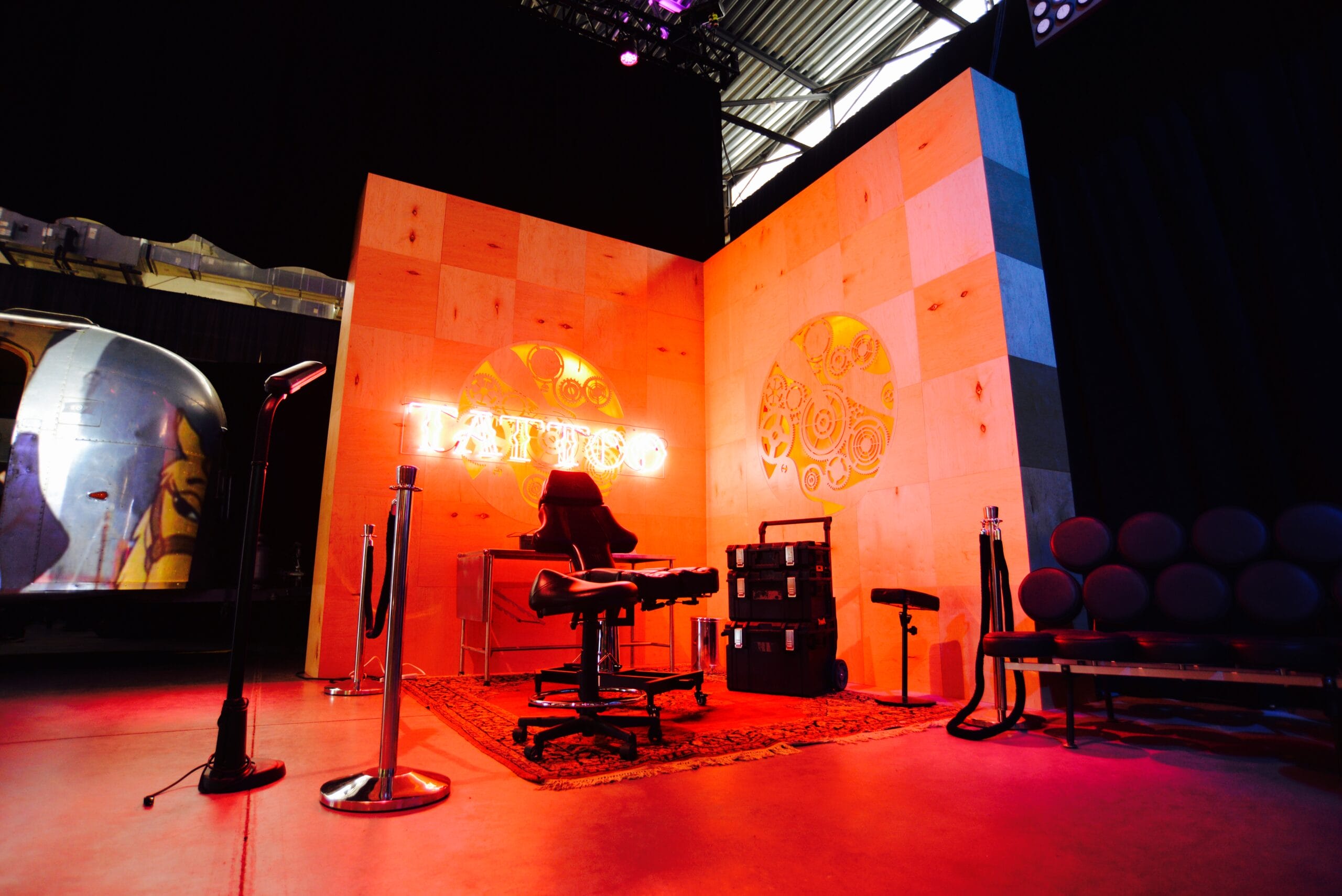 Tattoo parlor setup with neon sign, tattoo chairs, and a couch.