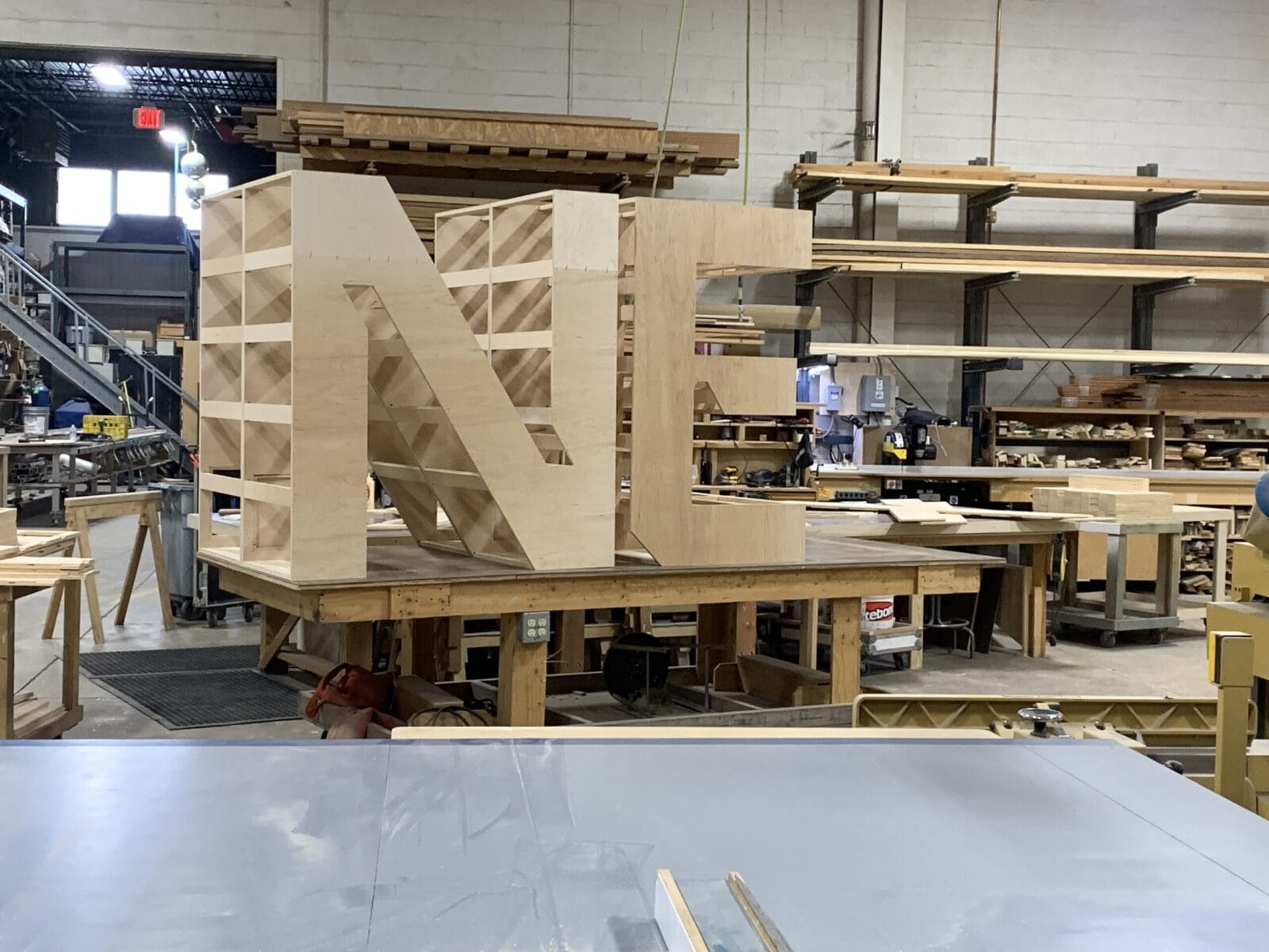 Large wooden letters "N" and "F" under construction in a workshop.