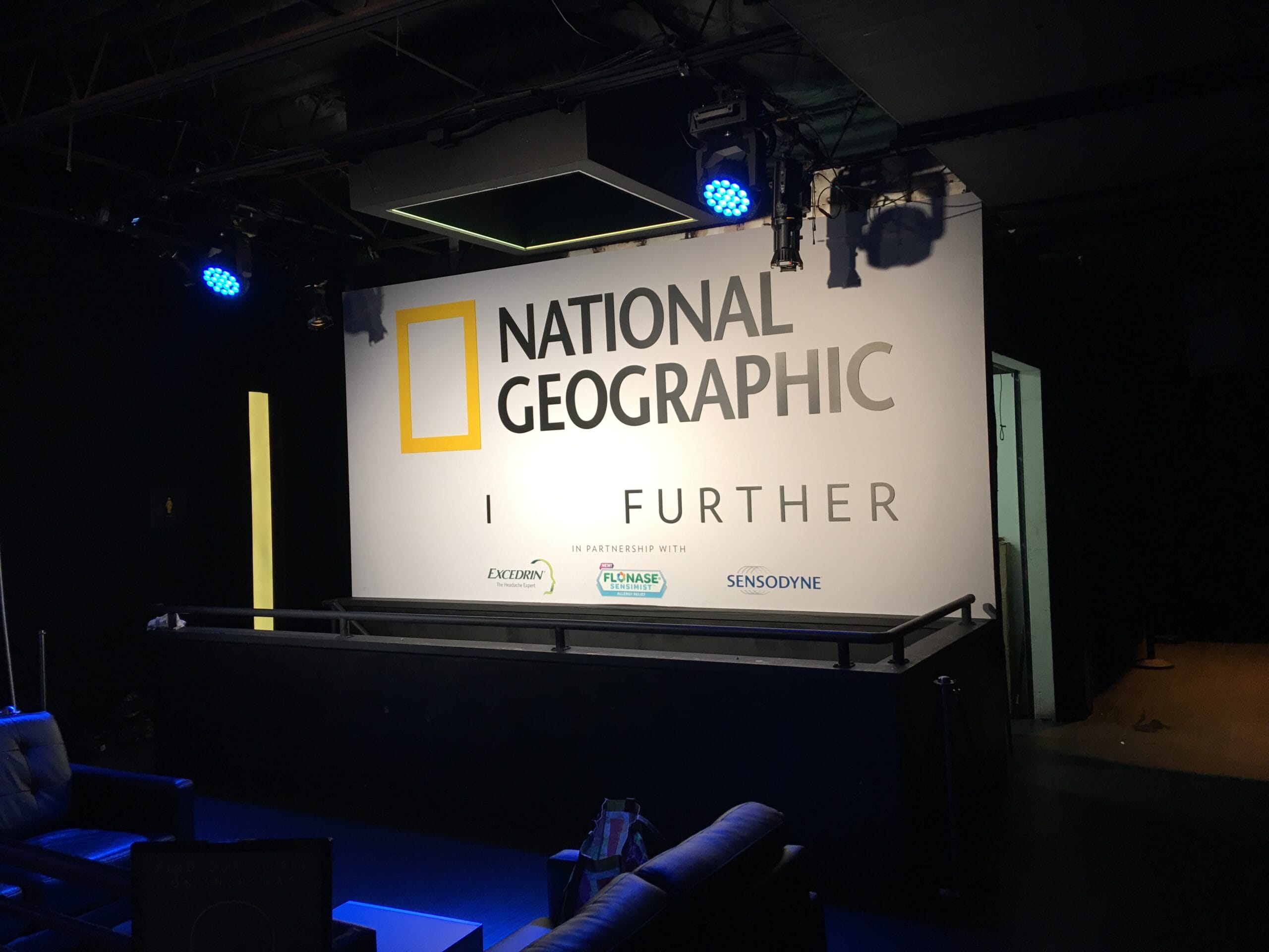 National Geographic "I FURTHER" banner with sponsor logos, stage lighting.