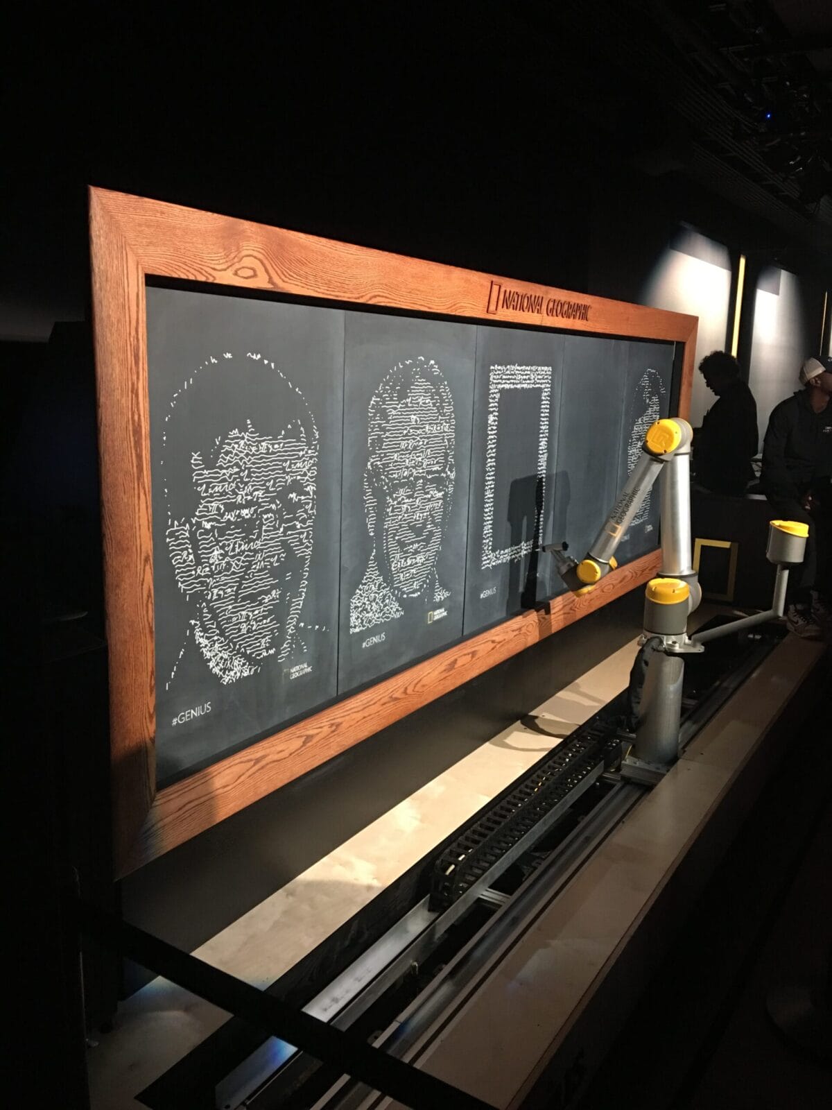 Robotic arm drawing portraits on a National Geographic chalkboard exhibit.