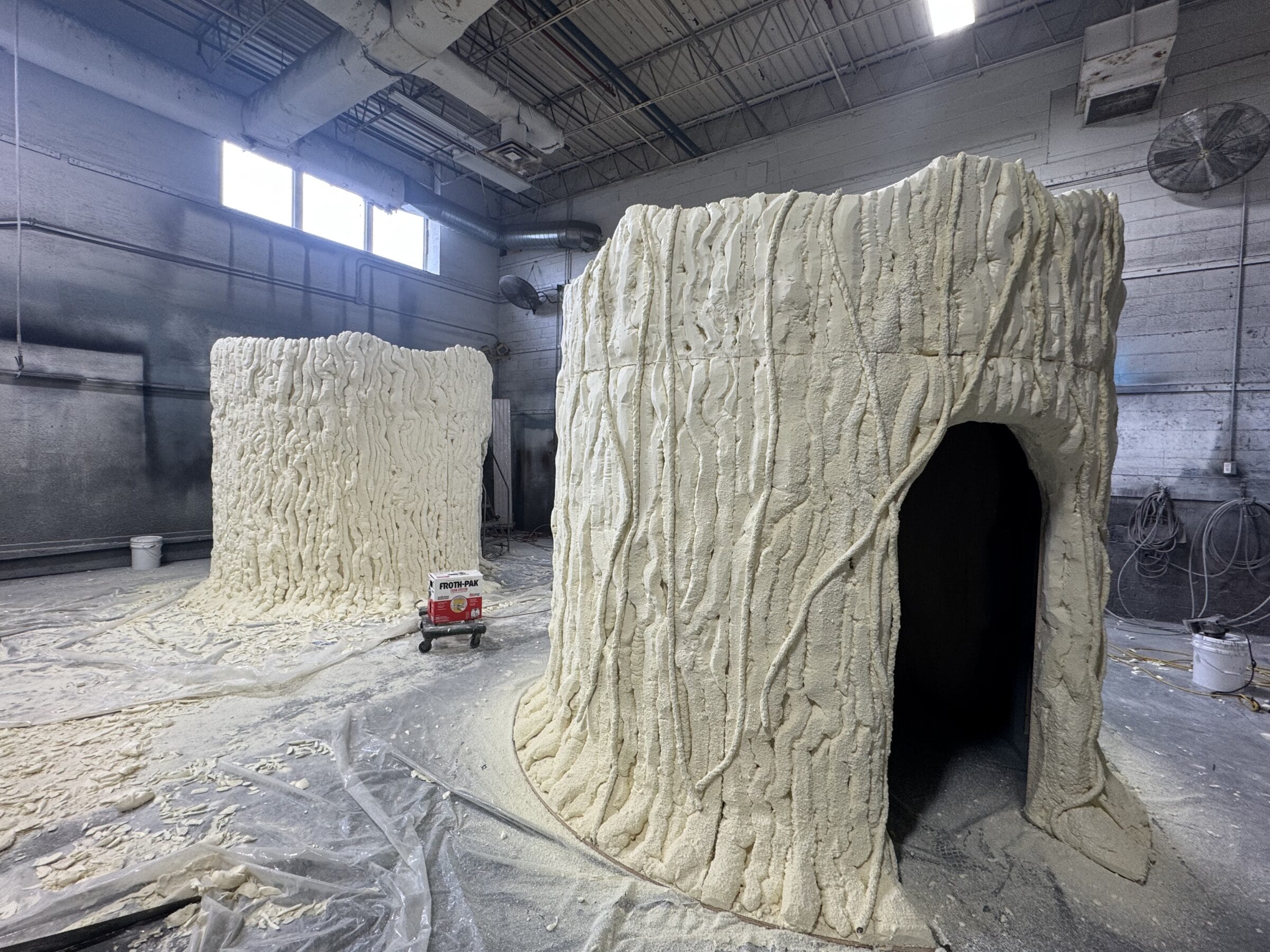 Two large, unfinished foam tree trunks with entrances in a workshop.