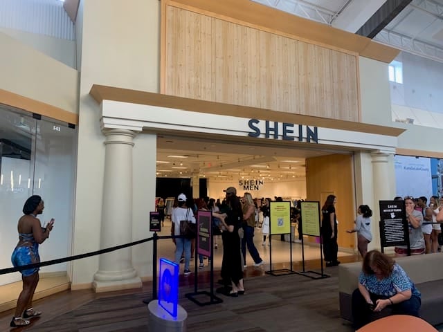 Shein store entrance with a line of people and a woman taking a photo.