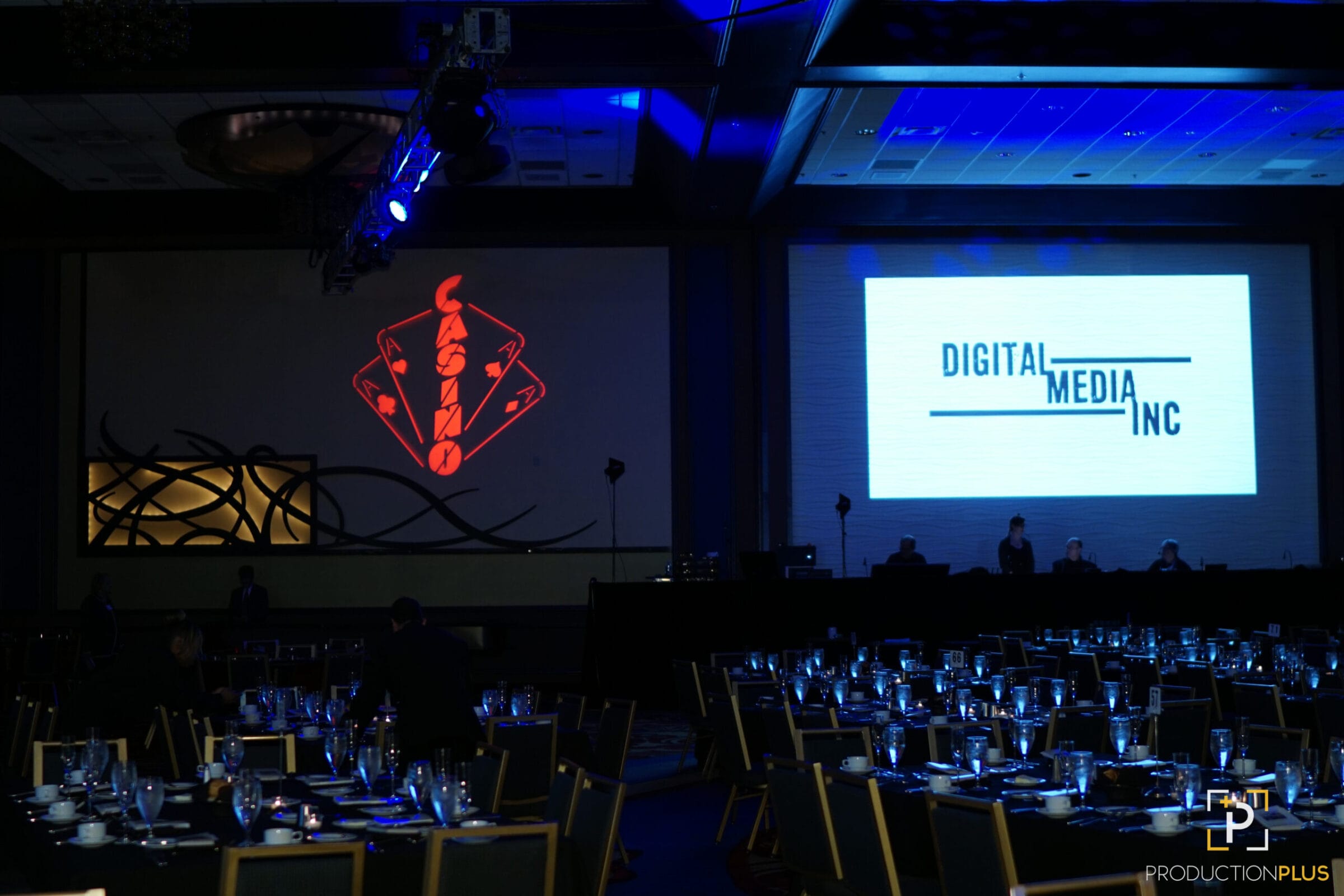 Casino logo and Digital Media Inc. logo projected on screens in a dimly lit banquet hall with tables set.