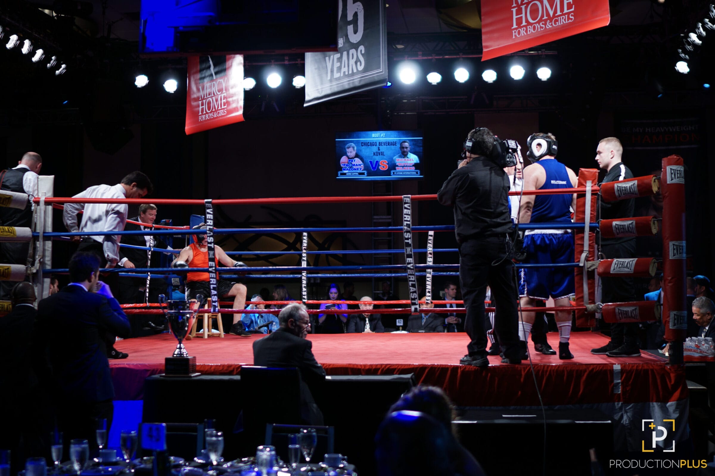 Boxing ring with fighters, officials, and a cameraman.