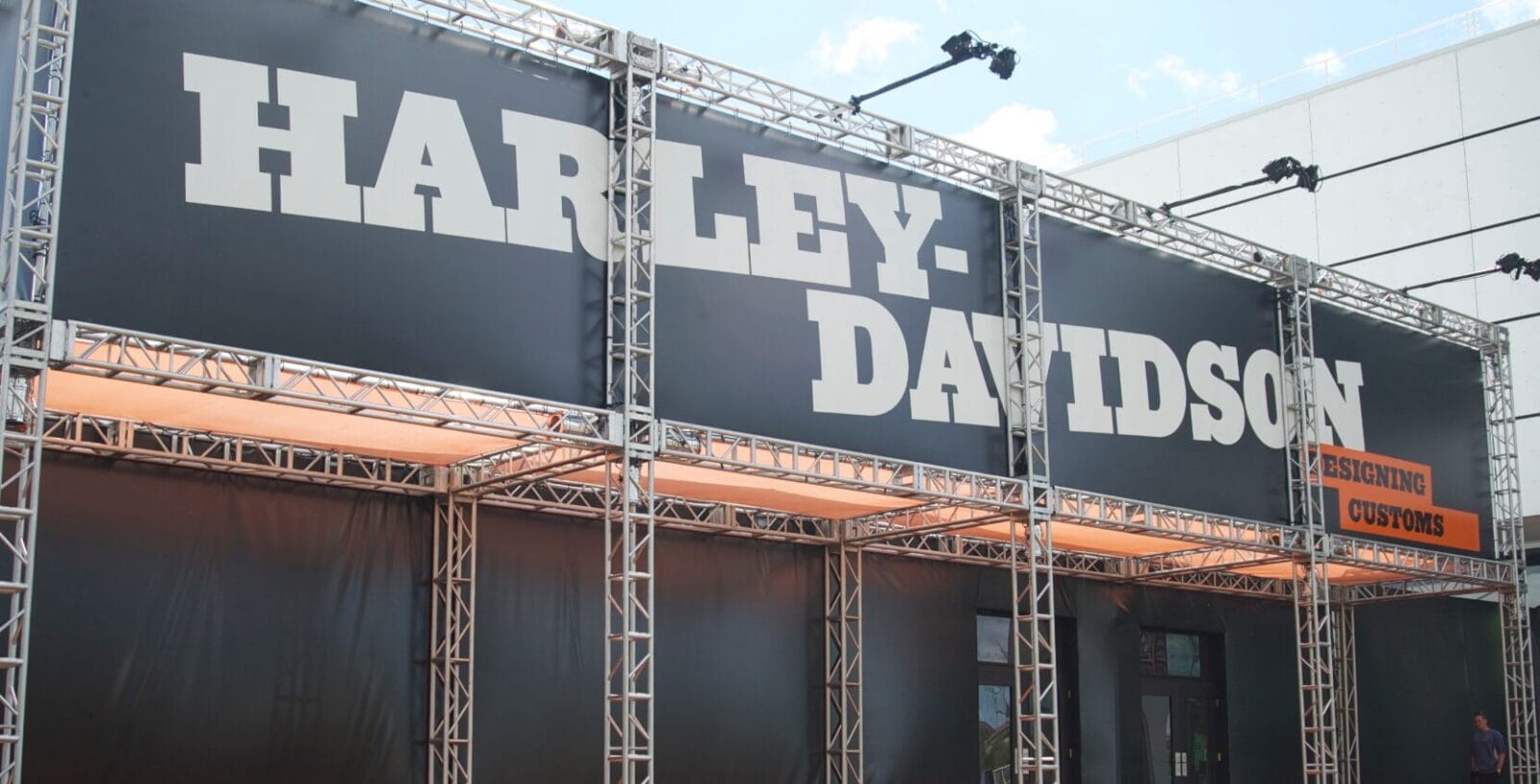 Harley-Davidson logo on a black banner with truss structure and orange accents.