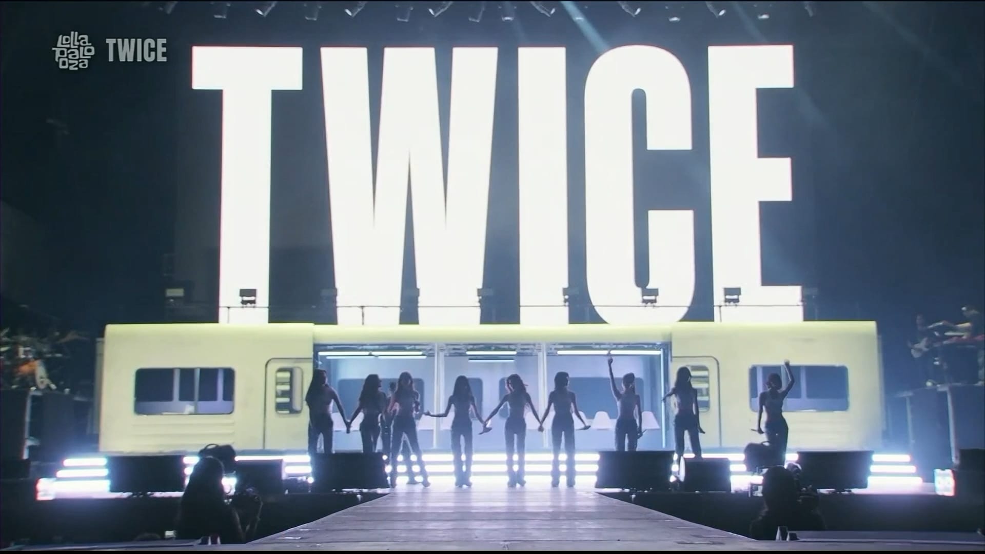 K-pop group TWICE performs on stage with a large "TWICE" logo and a train-like set.