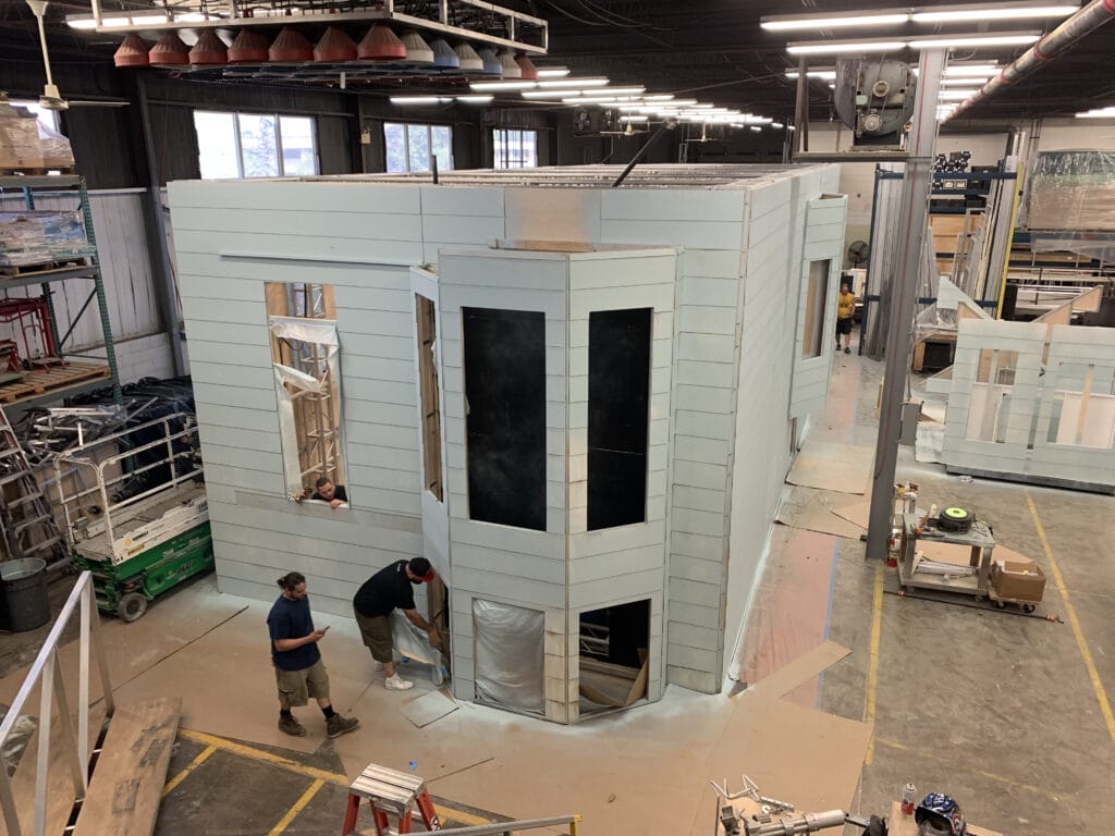 Construction workers build a light blue facade of a house in a warehouse.