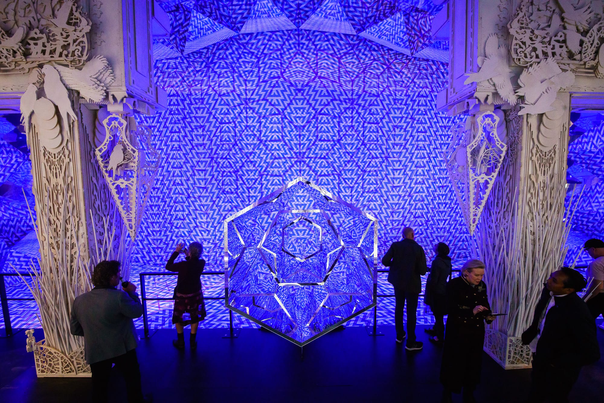 Geometric blue light installation with people observing.